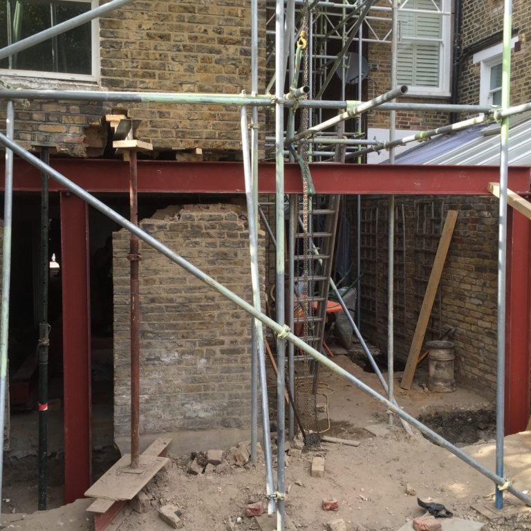 Construction site with scaffolding and a steel beam framework in progress. Creating an opening in the back of a house 